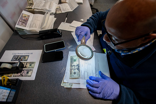 Secret Service forensics specialist looking closely at a $20 bill