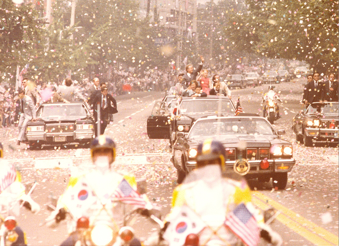 Special agents ride on the outside of limos as President Carter waves to the crowd in South Korea.