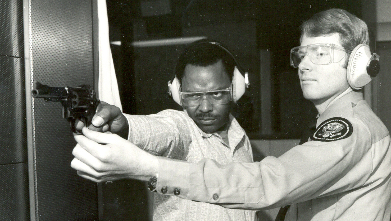 An instructor assists a student with firearms training in the 1970s.